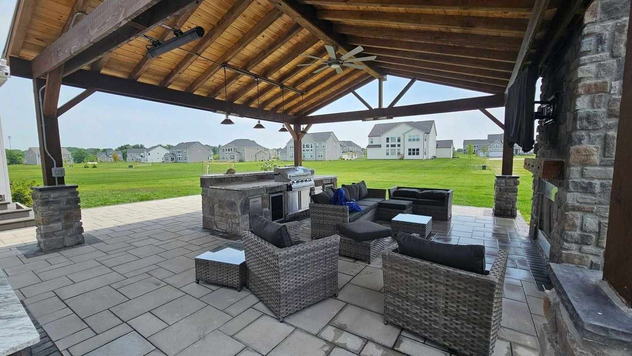 Lounge furniture under a cedar pavilion with a tongue-and-groove ceiling and stone fireplace