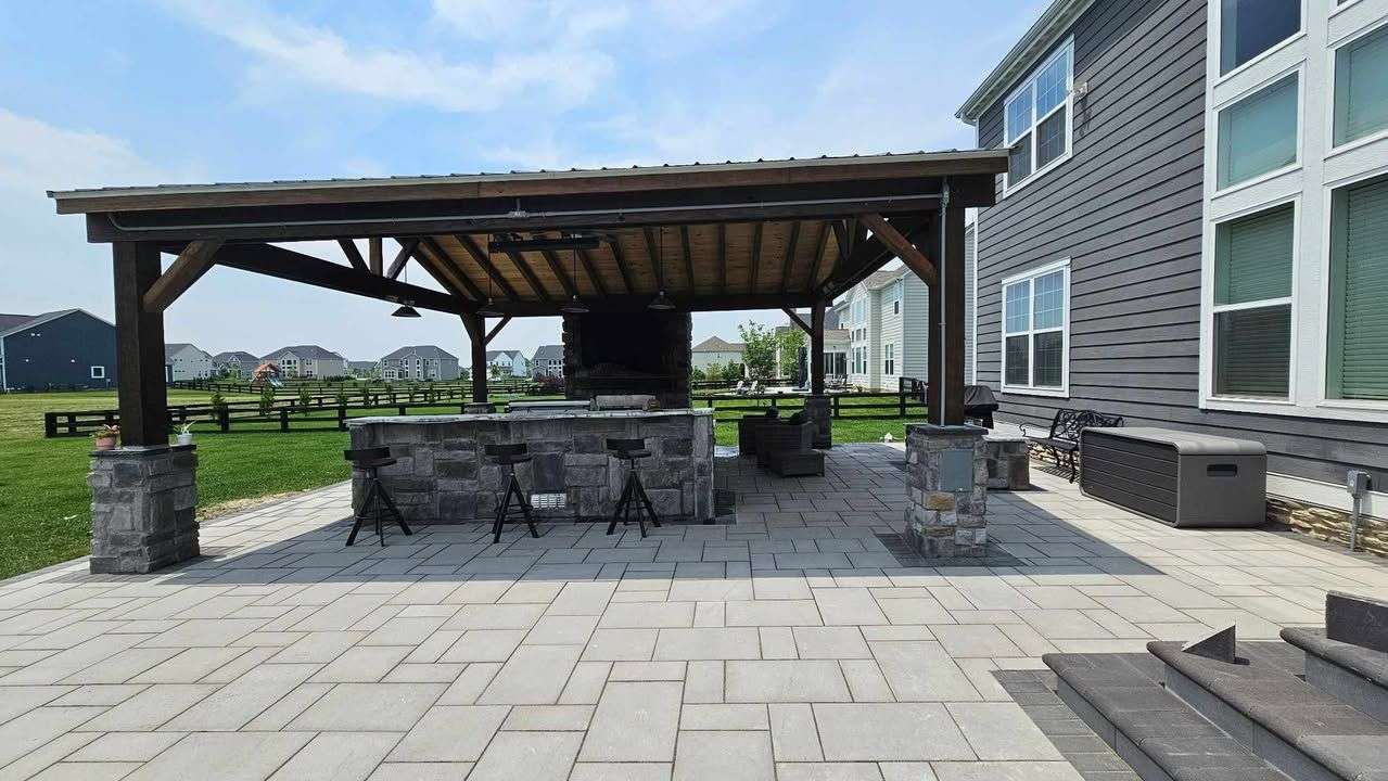 Cedar pavilion with a stone outdoor kitchen, bar seating and paver patio