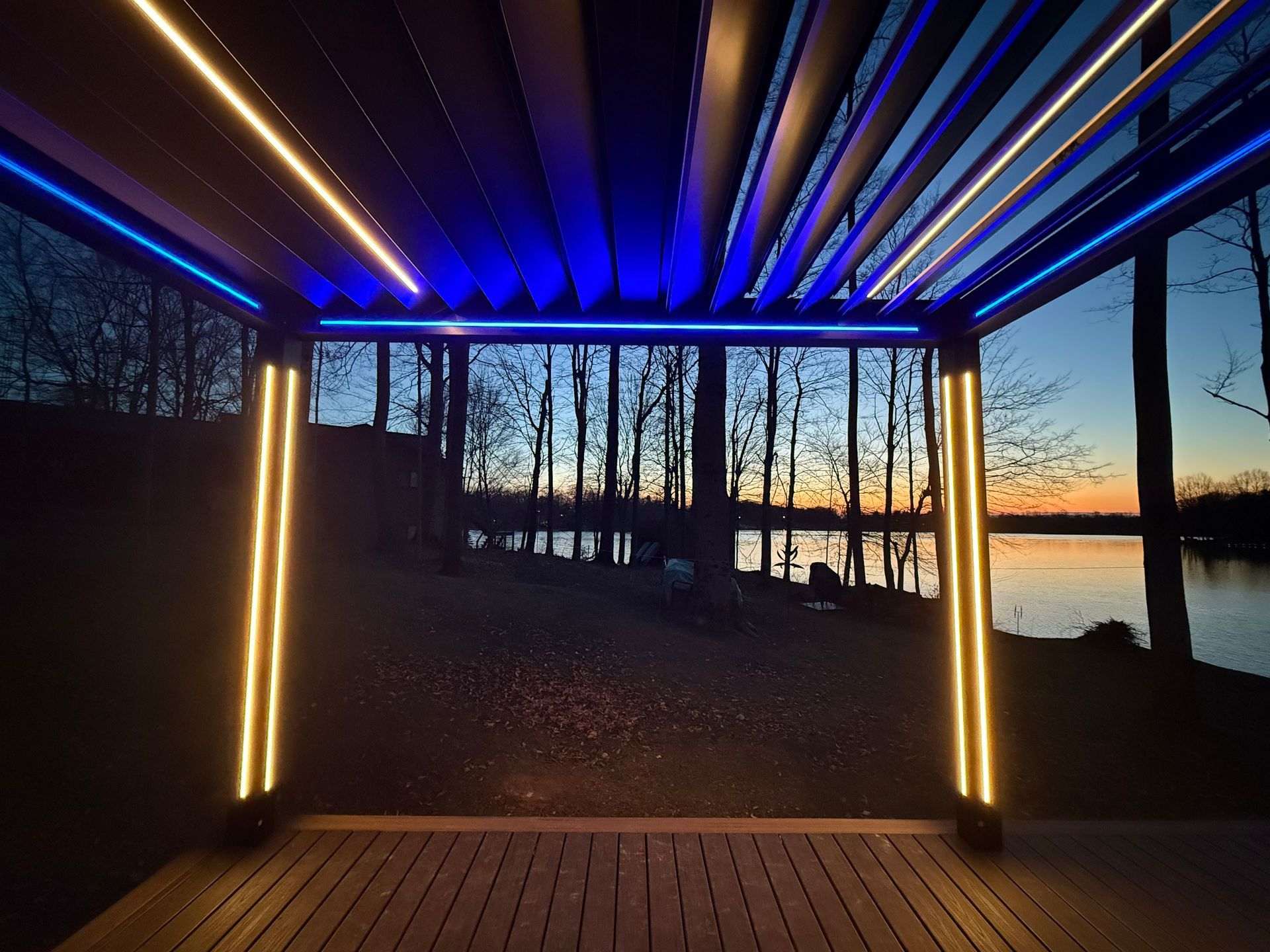 Underside of a motorized louvered pergola glowing with blue LED lighting at dusk